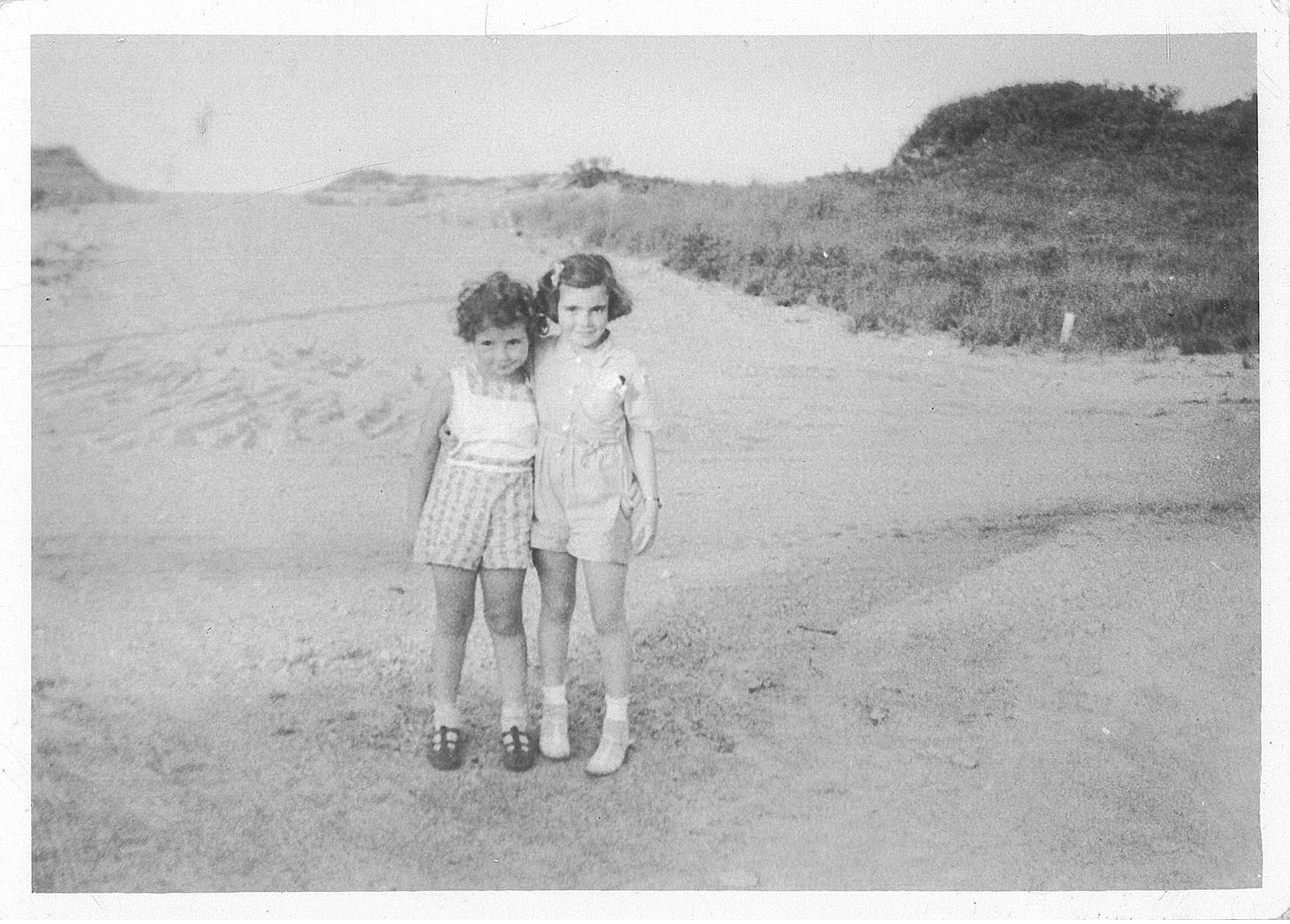 Two sisters dressed in their seersucker, cotton and lace summer playclothes, in the 1940's in the dunes of Swifts Beach in Wareham, Massachusetts